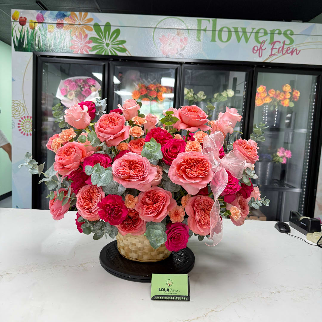 Basket arrangement of pink and coral roses with a sheer ribbon