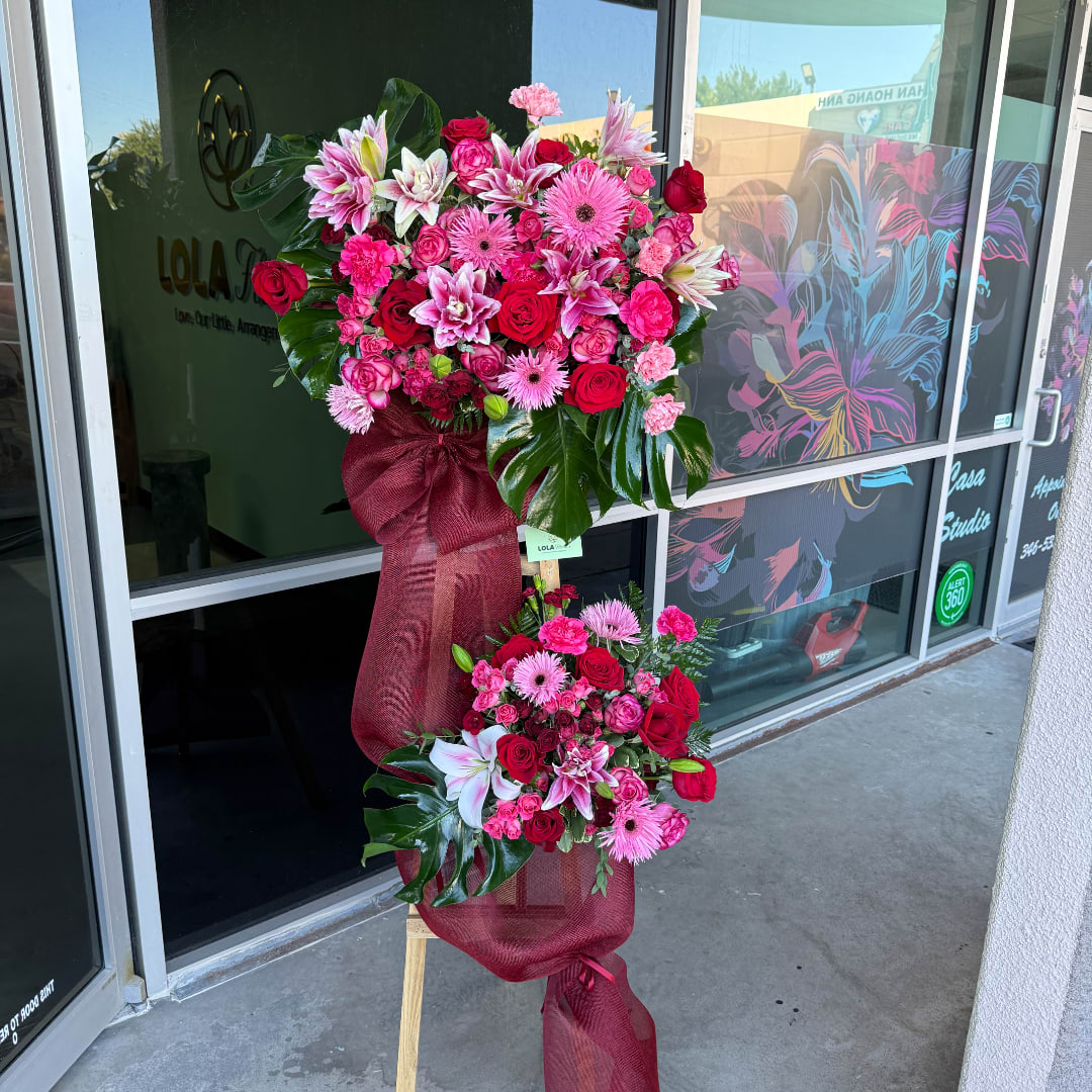 Two pink and red floral standing sprays on easels with burgundy ribbon