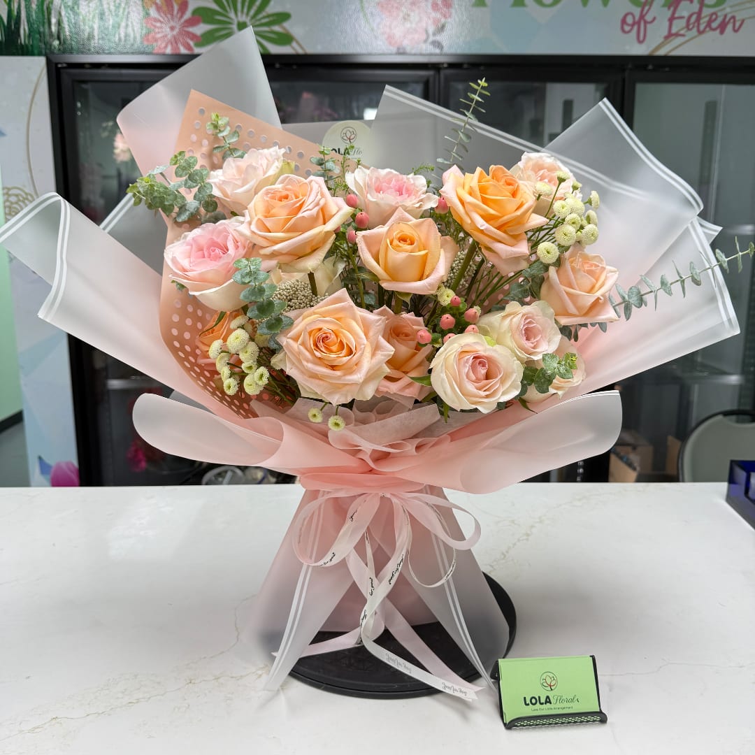 Bouquet of peach and pink roses wrapped in pale pink paper