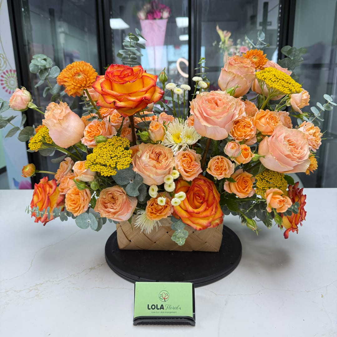 Peach and orange rose arrangement in a woven basket with yellow accents