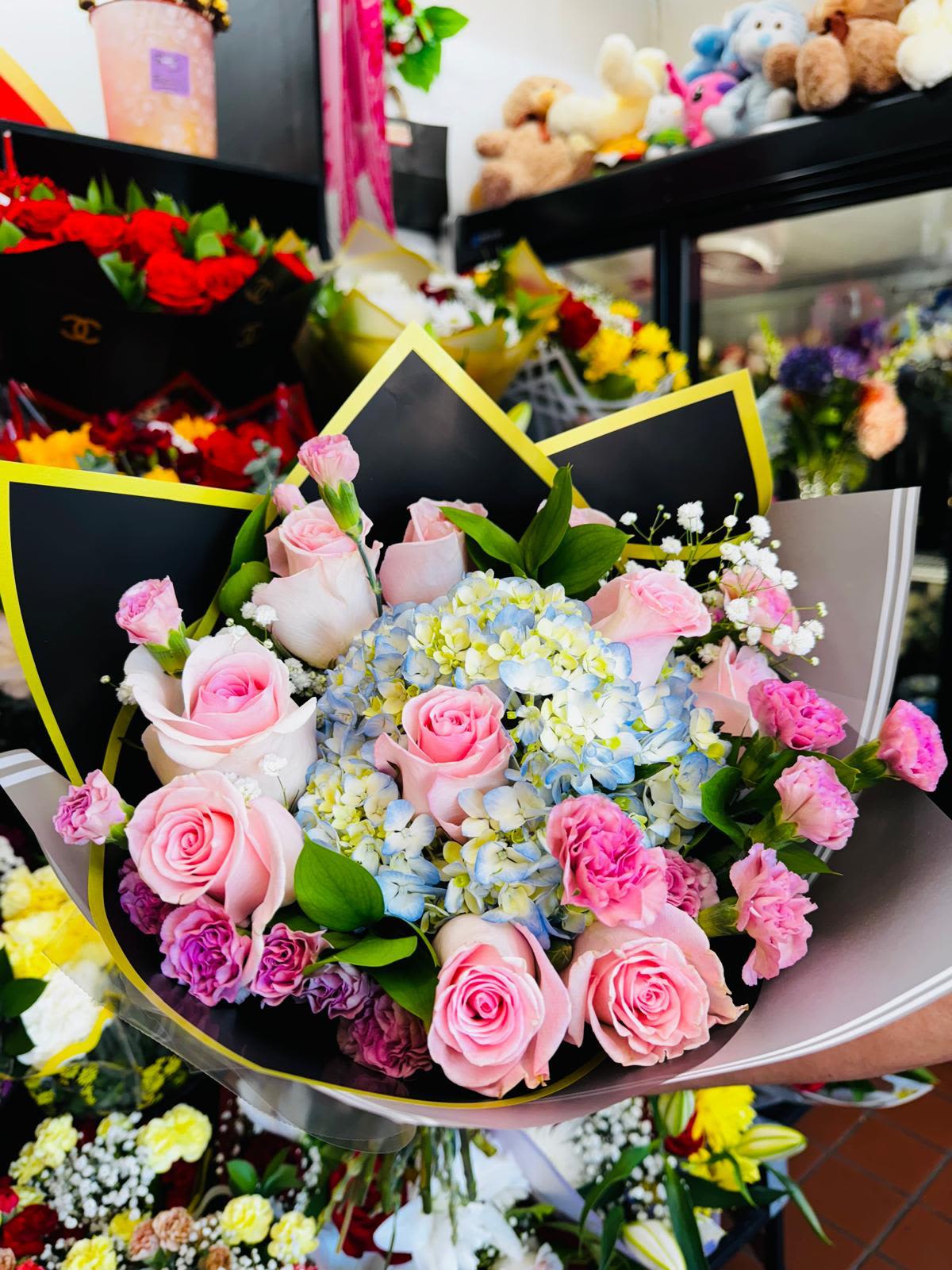 Hand-tied bouquet of pink roses and sprays with blue and white hydrangeas in decorative wrap