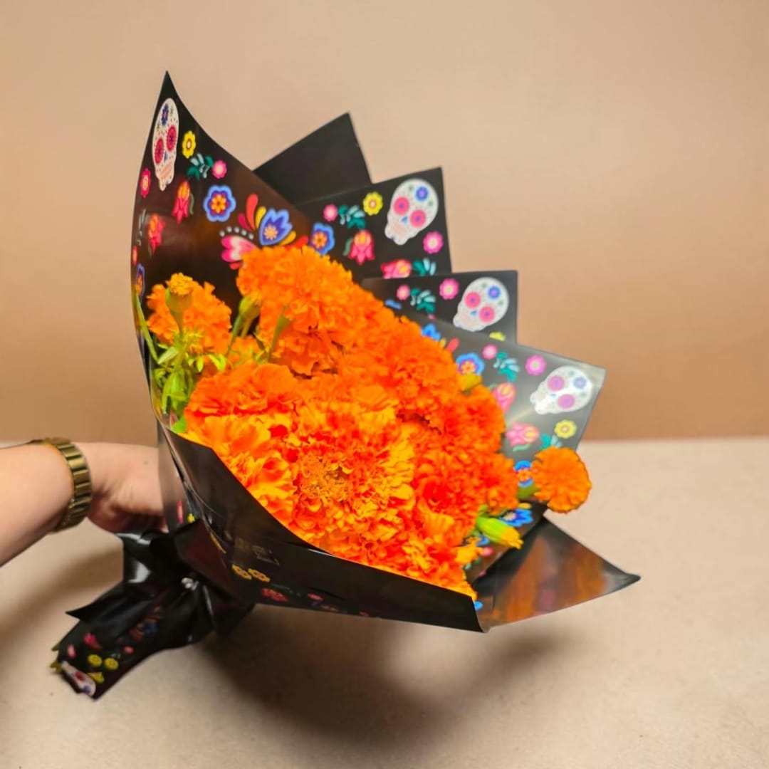Orange marigold bouquet wrapped in black paper with colorful skull prints