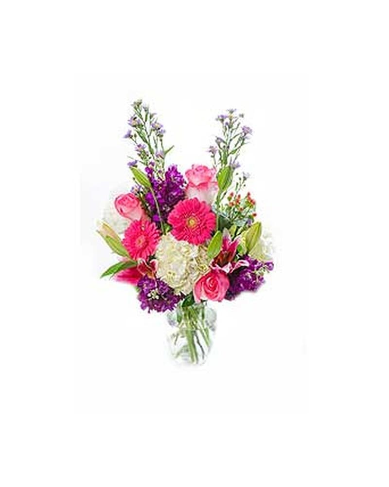 Bright mixed bouquet of pink gerbera daisies, roses, and white hydrangea in a clear glass vase