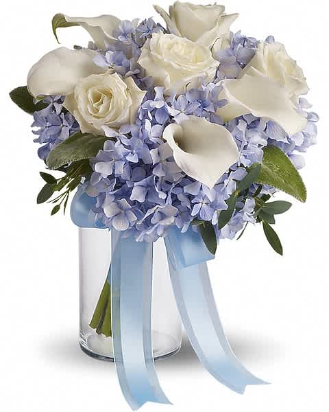 White roses and calla lilies with light blue hydrangeas in a clear vase with blue ribbon.