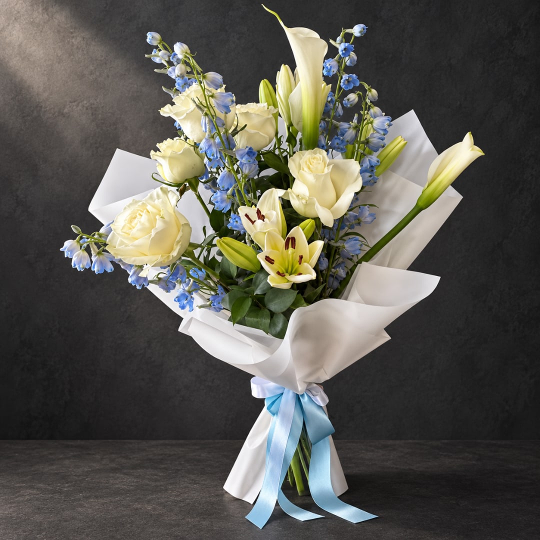 Bouquet of white roses, lilies, and blue flowers wrapped in white paper