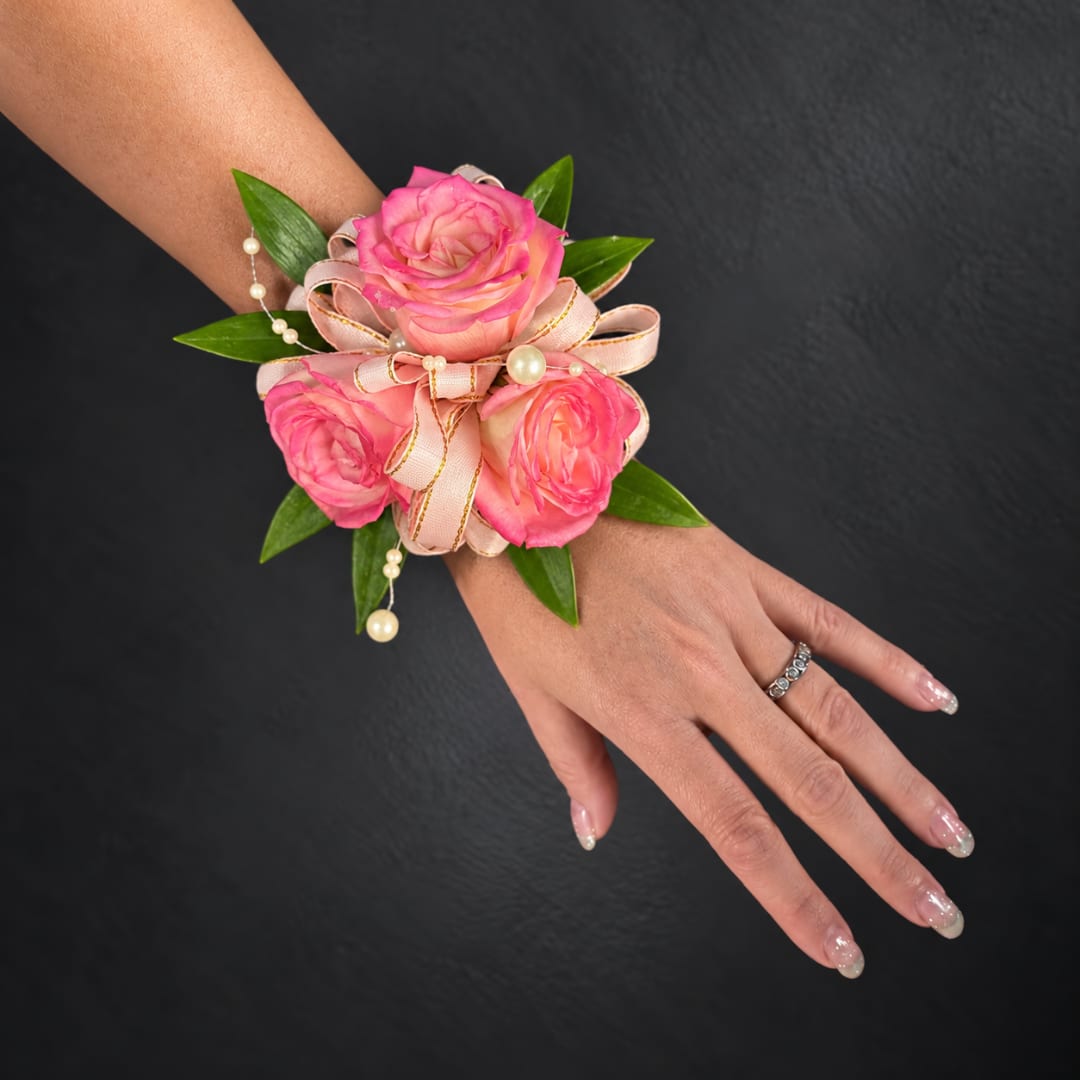 Pink rose wrist corsage with ribbon and pearl accents on a hand