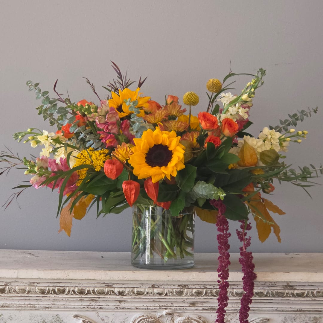 Mixed bouquet with sunflowers, orange roses, and white blooms in a glass vase
