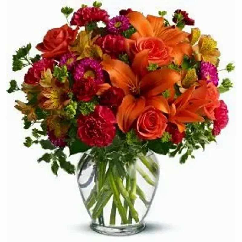 Bouquet of orange lilies, red roses, and mixed flowers in a clear glass vase