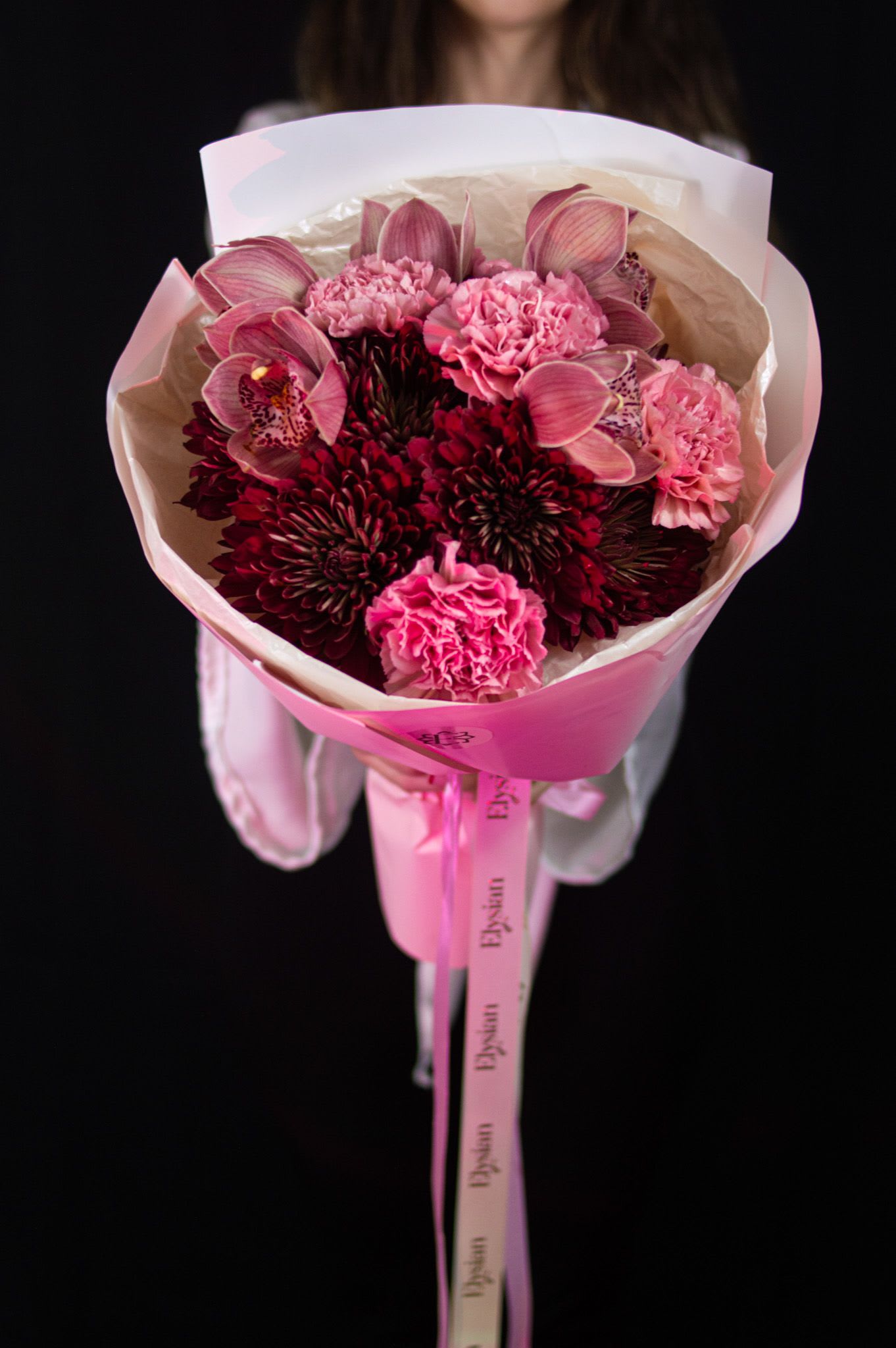 Soulmate - Deep burgundy blooms, soft blush carnations, and elegant orchids come together in a rich, romantic harmony—bold yet tender. Soulmate is made for moments when emotions run deep, and words fall short.  Because true love is felt, not explained.  Disclaimer: Due to the seasonal nature of flowers, we take the liberty of selecting the freshest blooms available. Flower varieties may vary, but we always ensure the arrangement maintains the same color palette, style, and overall aesthetic.