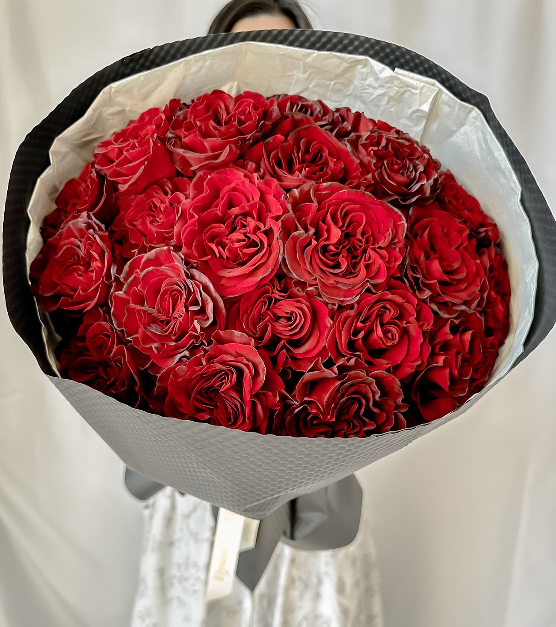 Red Hearts - Express your love with the Red Heart Bouquet, a breathtaking creation that will leave everyone speechless. It features 24 exquisite big-bloom red roses, each hand-selected for its velvety red hue and captivating dark accents on the petal tips. Every rose blossoms into the perfect heart shape.  Wrapped in premium materials and tied with an elegant ribbon, it’s the ultimate statement of love for Valentine’s Day.  Premium Rose Availability Disclaimer  Certain premium rose varieties, such as Red Heart roses, require a minimum of 5 days advance booking to ensure availability and the highest quality.  We kindly recommend placing your order in advance if you wish to include these exclusive blooms in your arrangement. Last-minute requests may require substitutions with roses of similar beauty and value.