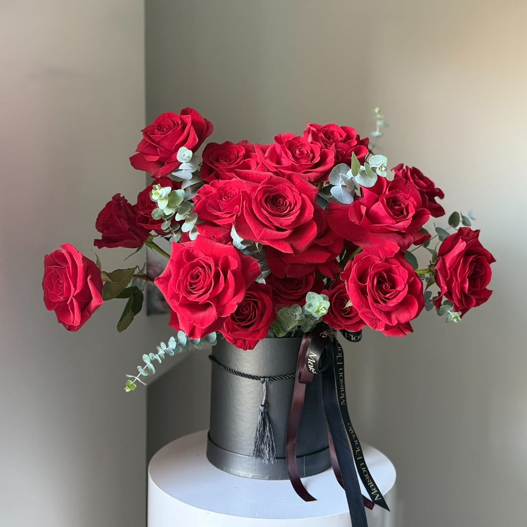 Red roses arranged in a black hatbox with ribbon accents