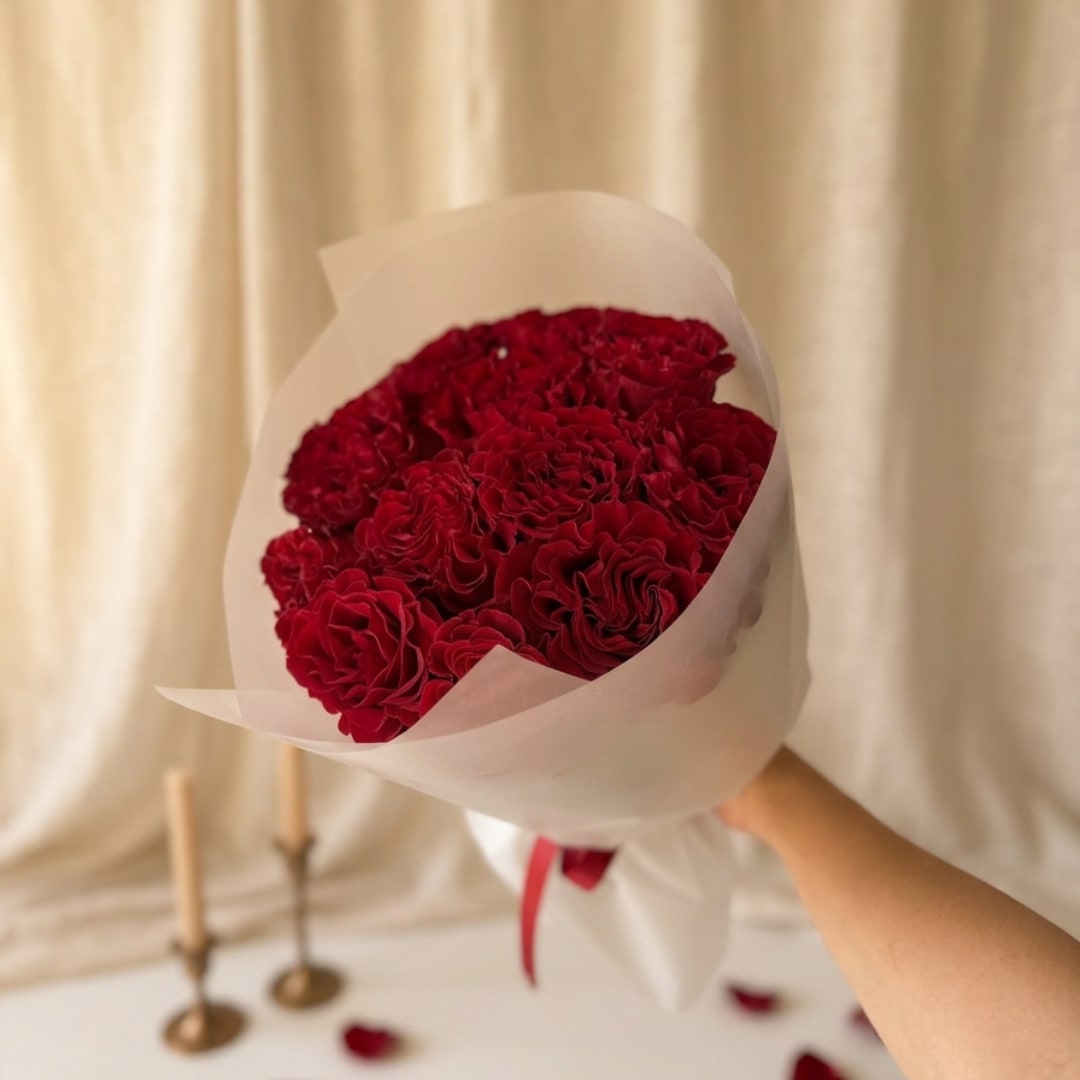 Handheld bouquet of red roses wrapped in white paper