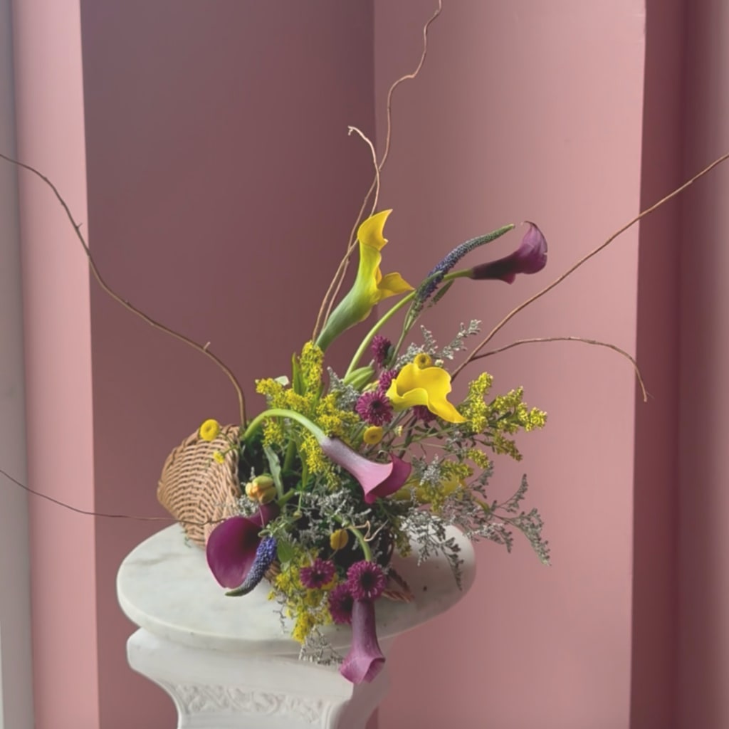 Colorful calla lily arrangement with tall branches in a woven basket