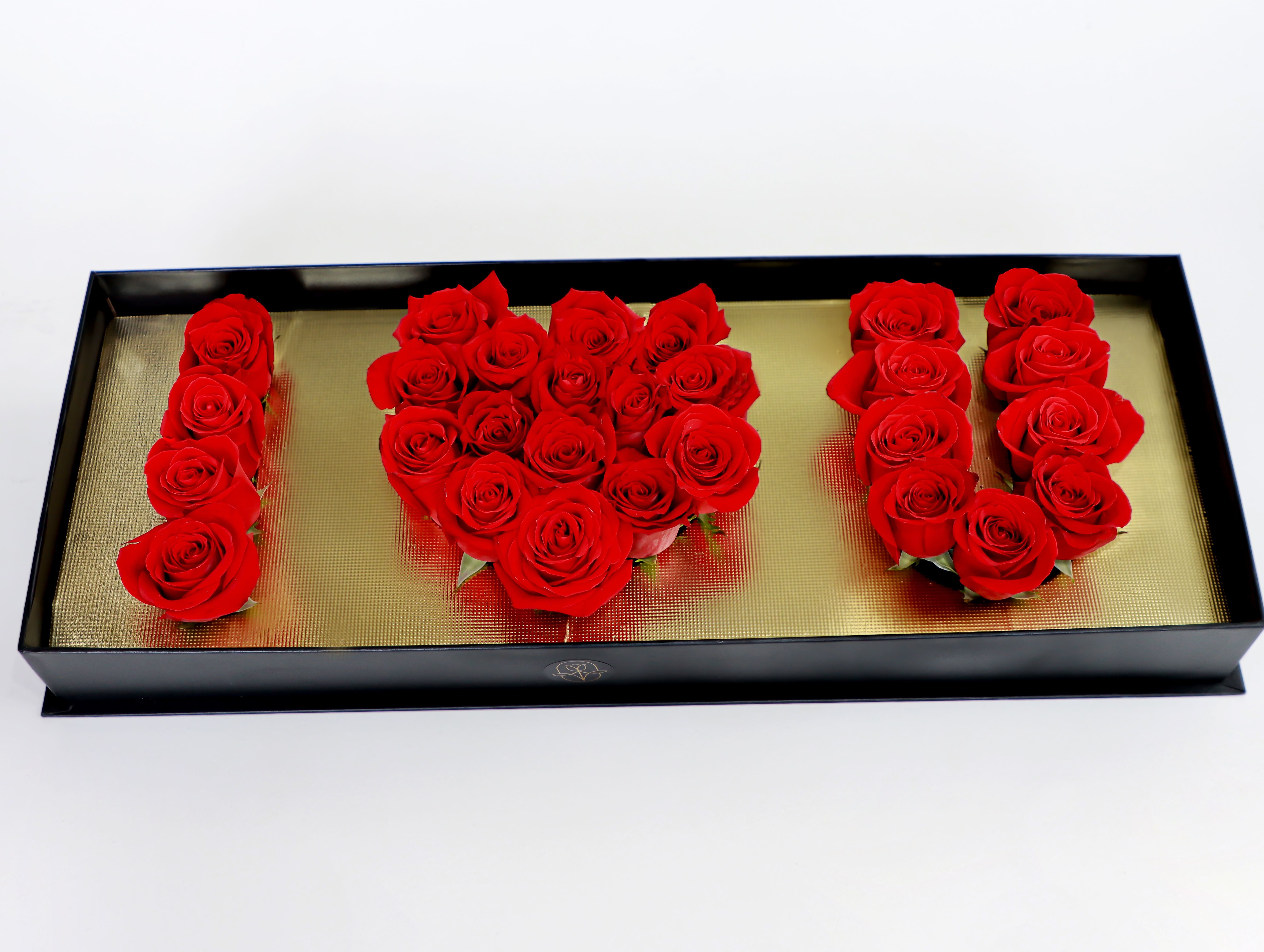 Crimson Love - A dramatic lineup of saturated red roses shaped into the number 100 makes a bold statement for anniversaries, milestone birthdays, or any congratulatory occasion where romance and celebration meet. This anniversary roses arrangement presents the recipient with an unmistakable message of devotion-she'll feel honored and deeply celebrated the moment the black rectangular box is opened and those vivid red blooms appear.  The roses are tightly grouped inside a long, elegant black gift box with a gold-toned base, the dark frame sharpening the color contrast and giving the arrangement a polished, gift-ready look. The compact rectangular profile makes it easy to display on a mantle or reception table; the contrast between lush, velvety petals and the metallic-looking background adds a luxe, tactile impression that reads as both modern and timeless.  Perfect for marking 100 days, a centennial milestone, or a heartfelt anniversary, this piece is designed to make the person you're thinking of feel truly seen and celebrated. Arrange delivery for the date you need and rest assured the boxed presentation arrives ready to gift - no additional wrapping required.