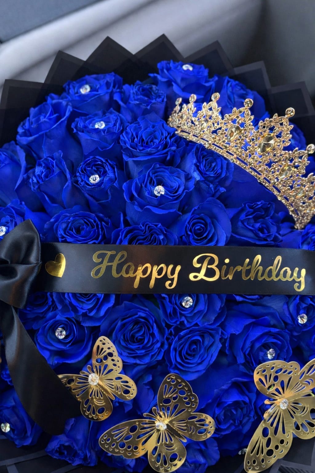 Royal Sapphire Crown Bouquet  - This breathtaking bouquet is the perfect blend of luxury and elegance. The vibrant blue roses create a bold and sophisticated look, beautifully enhanced by the delicate gold crown and butterfly accents. The black wrapping and ribbon with “Happy Birthday” in gold lettering add a refined, premium touch. Every detail is carefully crafted, making it an unforgettable gift for any special celebration. If you want to impress and make someone feel truly special, this bouquet is an exceptional choice.