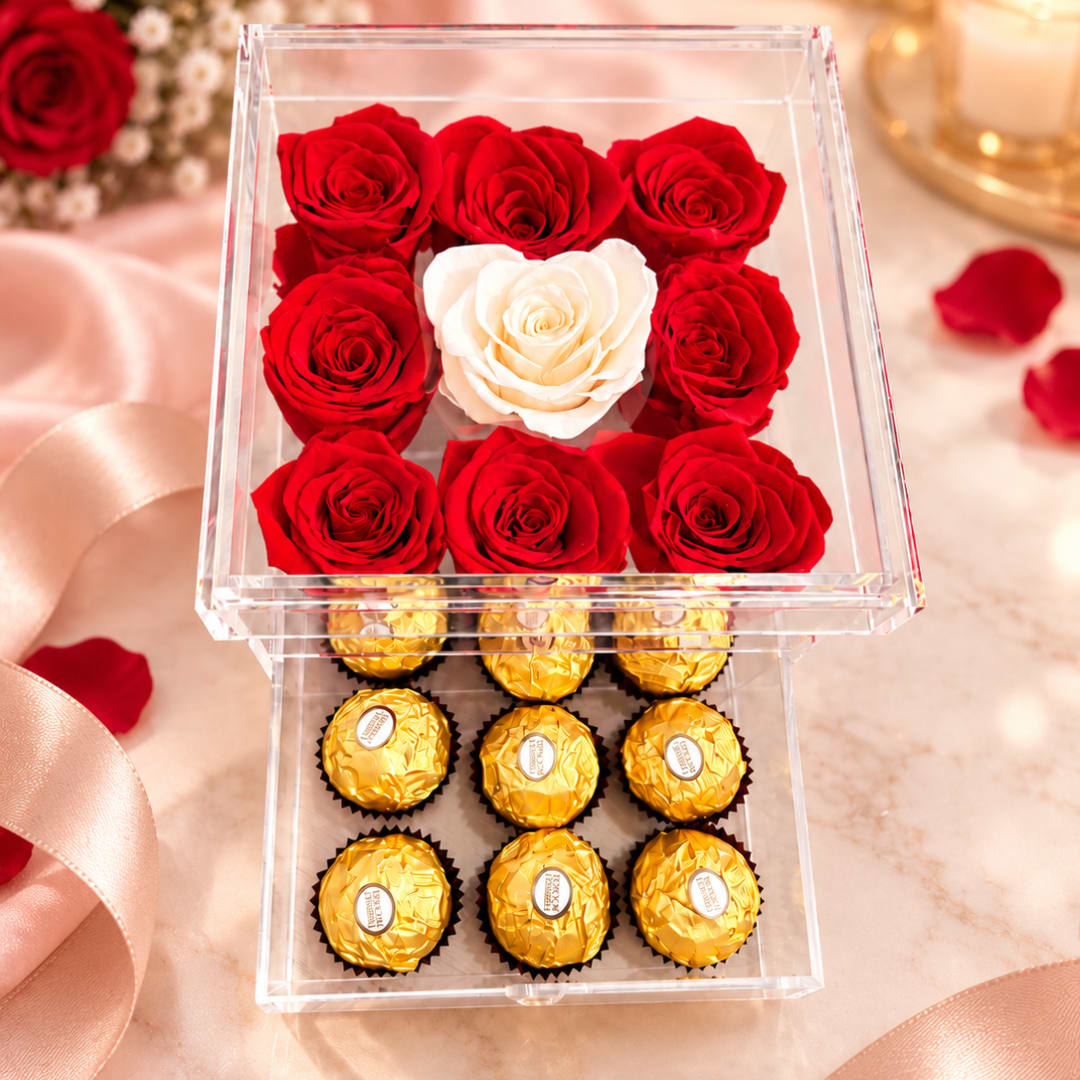Red and white roses in a clear box above gold-wrapped chocolates