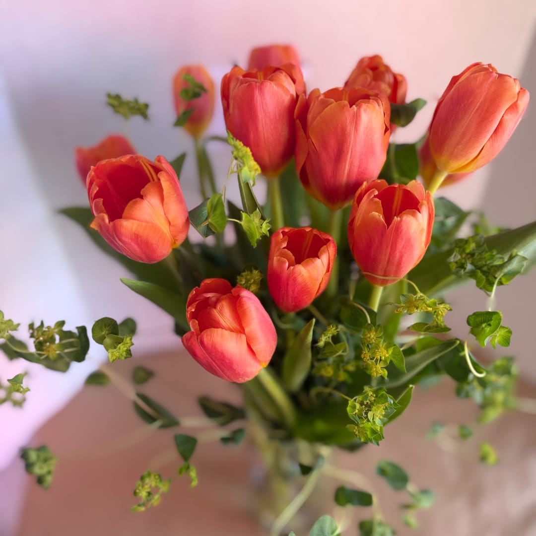 Orange-red tulips in a clear glass vase with scattered greenery
