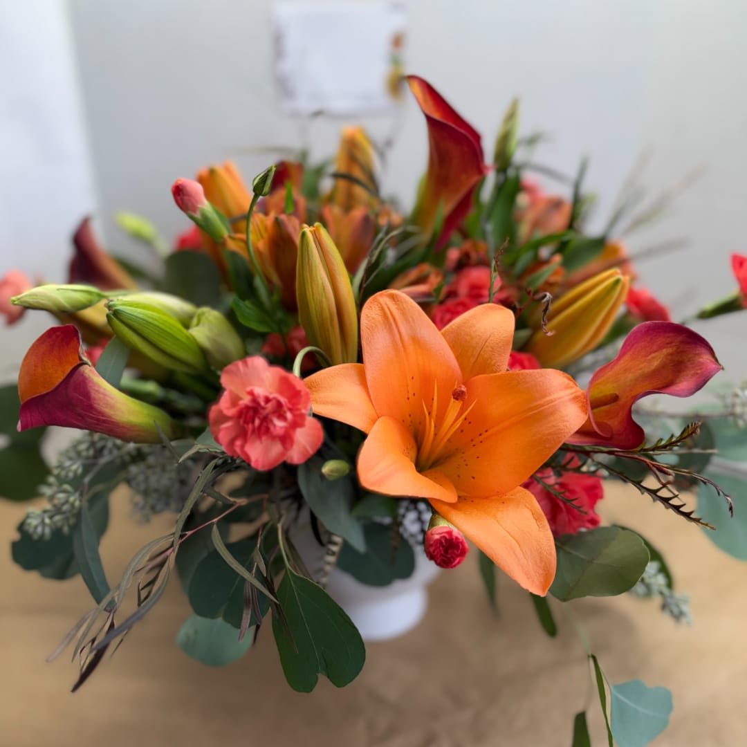 Orange lilies and calla lilies arranged in a white vase
