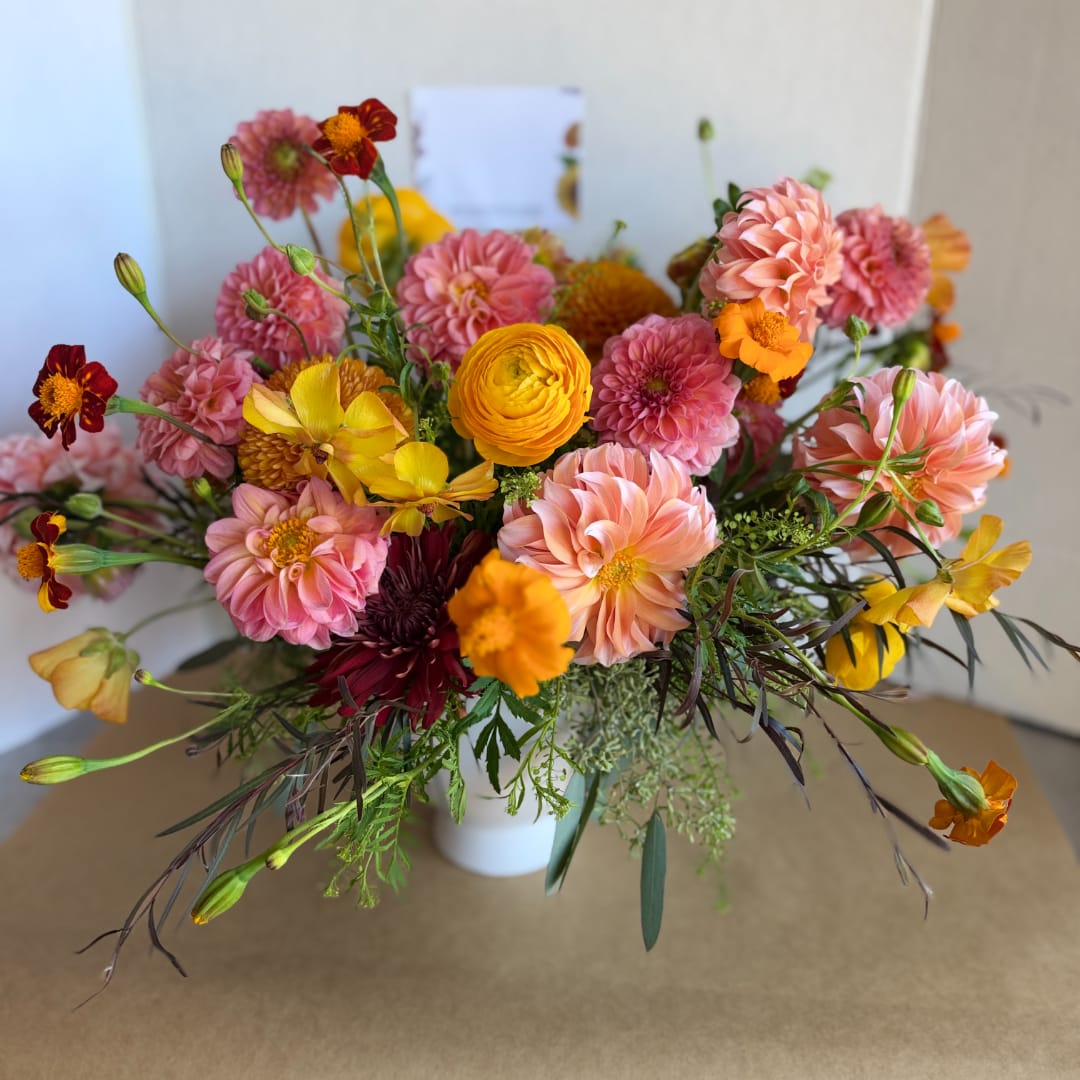 Mixed bouquet of pink, peach, yellow, and orange flowers in a white vase