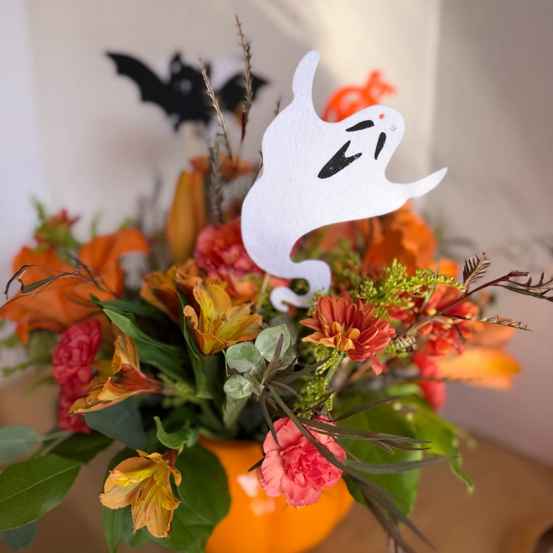 Halloween floral arrangement in an orange pumpkin container with a ghost topper