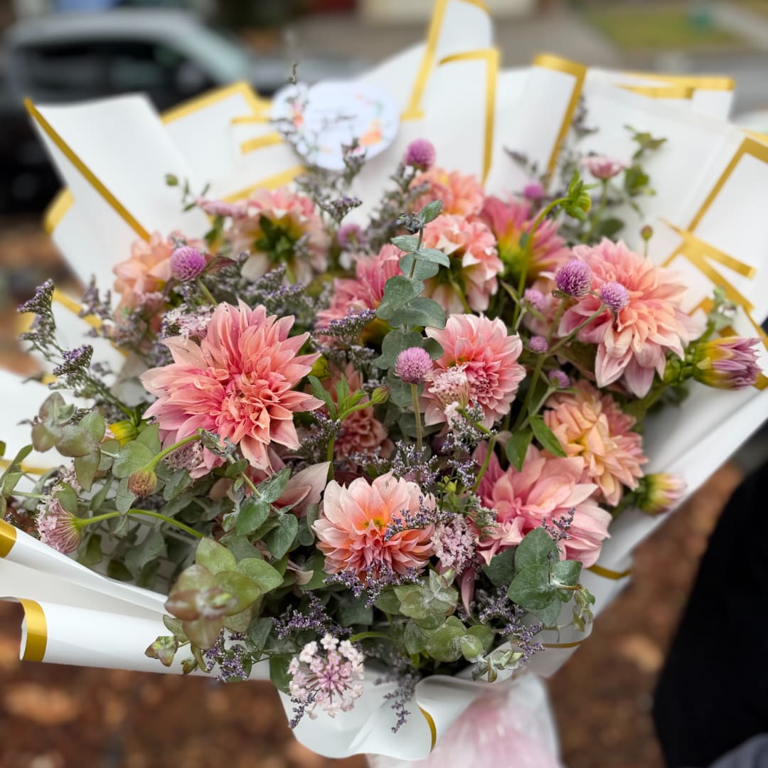 Pink dahlia bouquet wrapped in white paper with gold trim