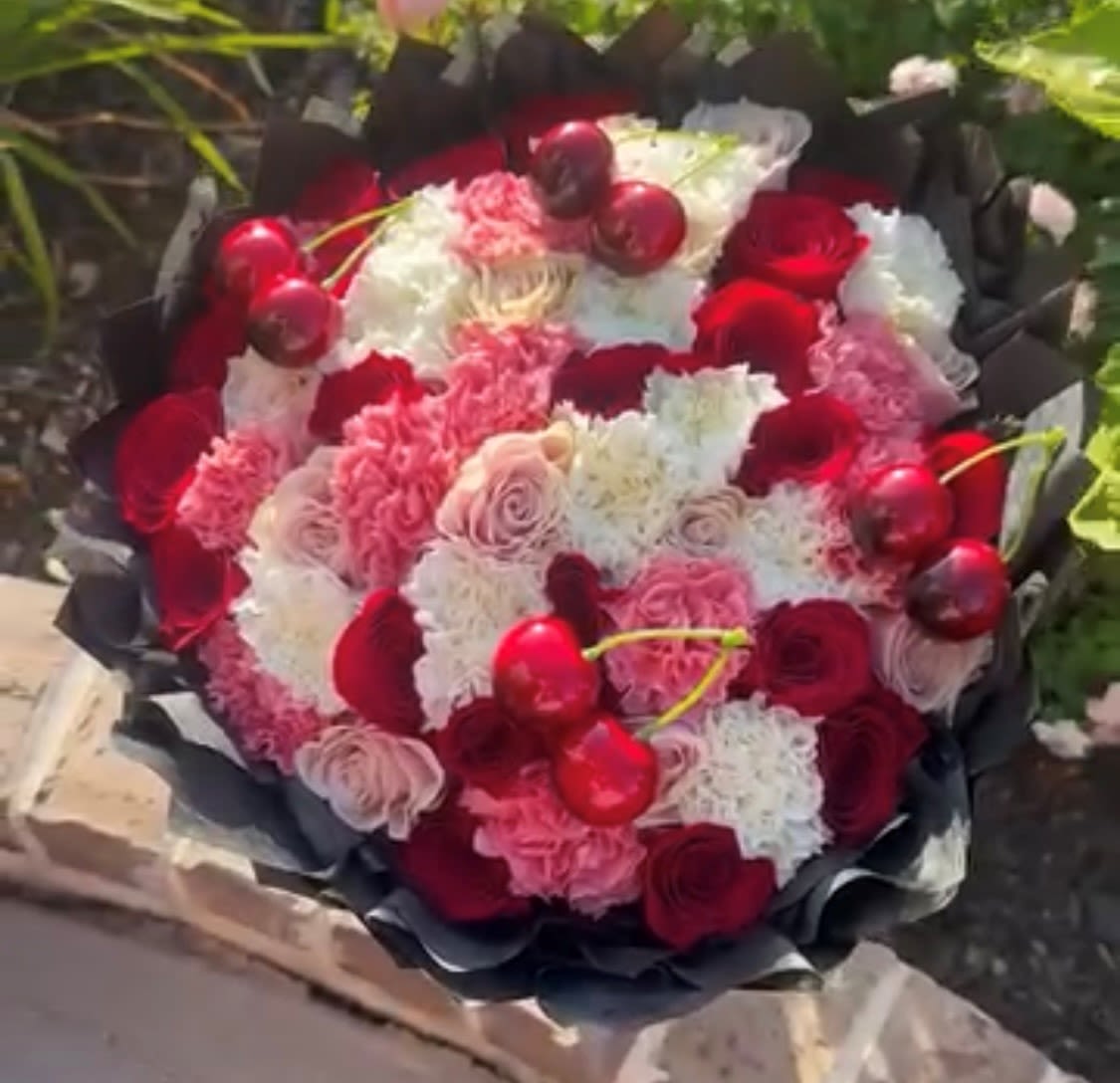 Cherry Delight - Crafted with red, pink, and white roses and carnations, the arrangement is arranged in a smooth, compact form so every bloom reads cleanly from every angle. A ruffled black paper wrap frames the bouquet, heightening the contrast and giving the colors a modern, dramatic pop. Lightweight decorative cherries add texture without overwhelming the petals, making this a memorable gift that reads romantic and fun.  