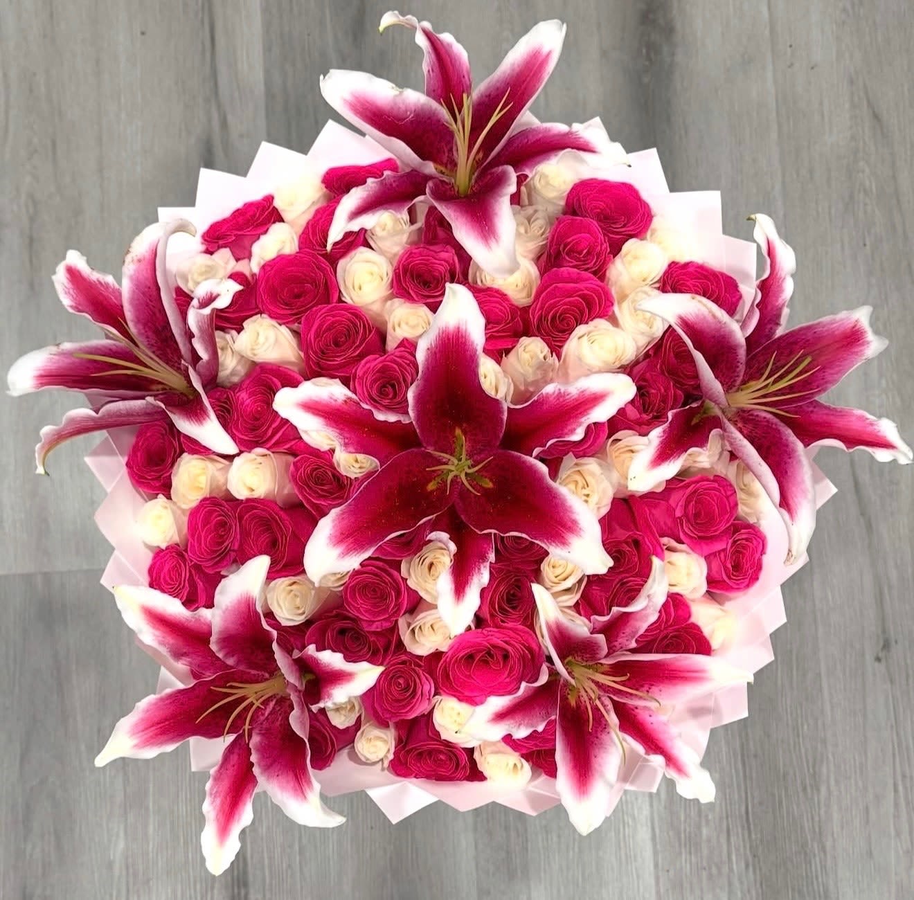 Lily Delight - Hot pink and white cream roses with lilies tipped in deep pink, arranged in a lush, rounded bouquet and wrapped in pale pink-and-white paper-bold, romantic and perfect for anniversaries.