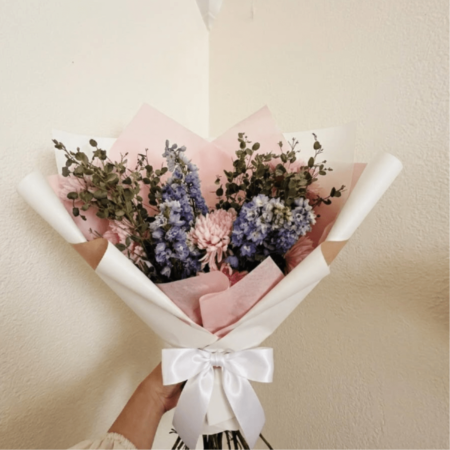 Trophy Bouquet - Regal, proud, and lush—Trophy Bouquet is fit for a winner. Bold blue delphinium and lavender mums create a sense of importance and pride for someone who has truly excelled in their field.  This seasonal bouquet features:  Lavender Cremone Mums  Light Blue Belladonna Delphinium  Fresh Boxwood  Garden Greens  Presentation: Expertly wrapped in our signature textured paper and tied with satin ribbon. Prefer a vase? Add one to your cart to complete the look.  Personal Touch: We’ll include a custom card message with every order. You’ll be able to write your message at checkout.  Please Note: All flowers are subject to seasonal availability. If a specific bloom isn’t available, our designers will thoughtfully substitute with flowers in a similar shape, style, and color.  Standard size shown. Vase upgrade is optional.   Floral Care Guide  Your arrangement arrives in our signature "double wrap" and is nestled in a protective box. While the stems are secured with a wet wrap for transit they are ready for a full drink!   Unpack: Gently lift the bouquet from the box. Remove the plastic bag and wet towel from the stems. Trim &amp; Hydrate: Trim 1/2" off stems at an angle and place in a clean vase with cool water. Refreshed: Change water daily for a long-lasting bloom.  
