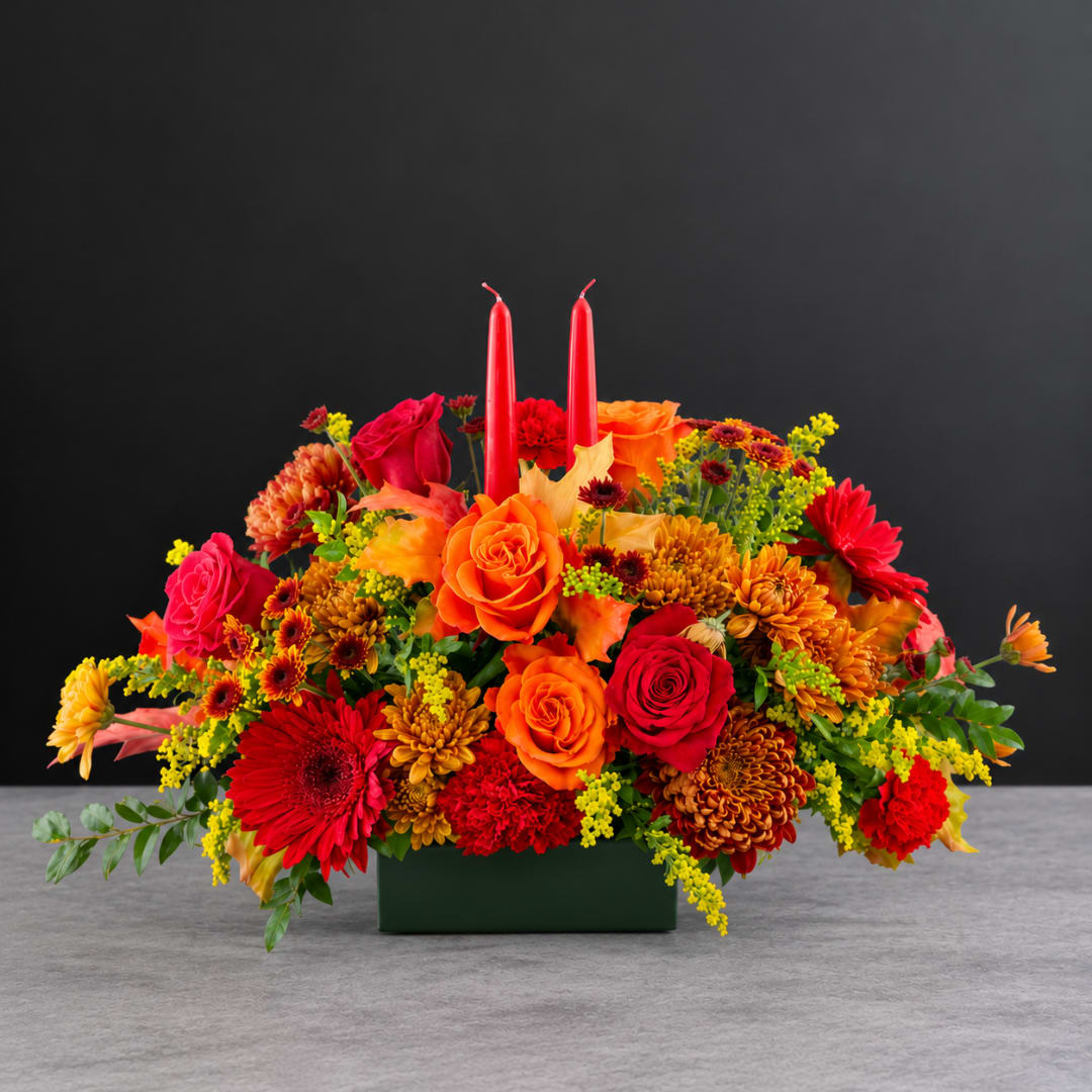 Bright mixed flower arrangement with red candles in a green container