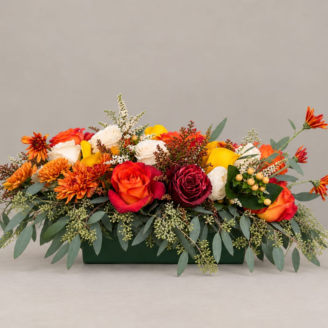 Low floral centerpiece with roses, mums, and yellow calla lilies in a green container