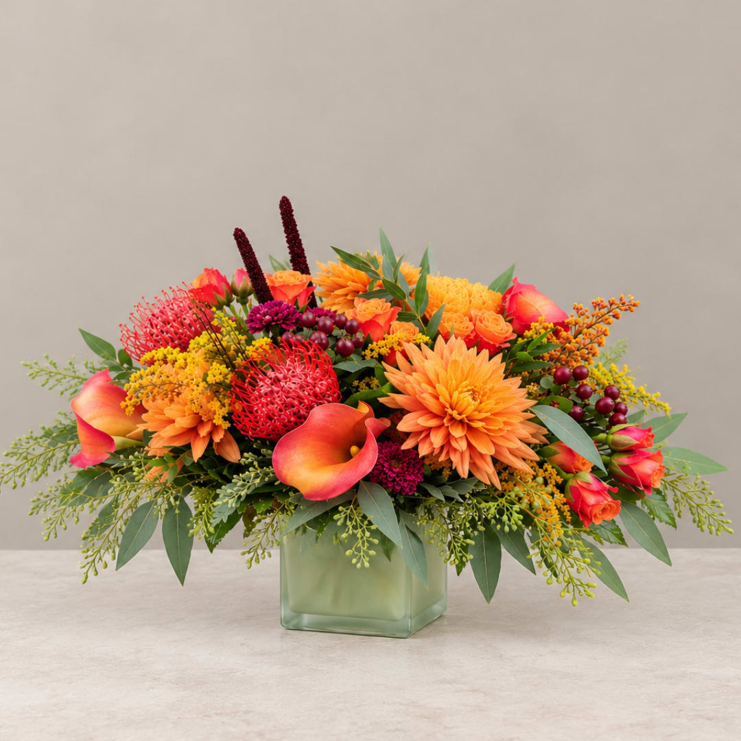 Bright orange and pink floral arrangement in a square glass vase