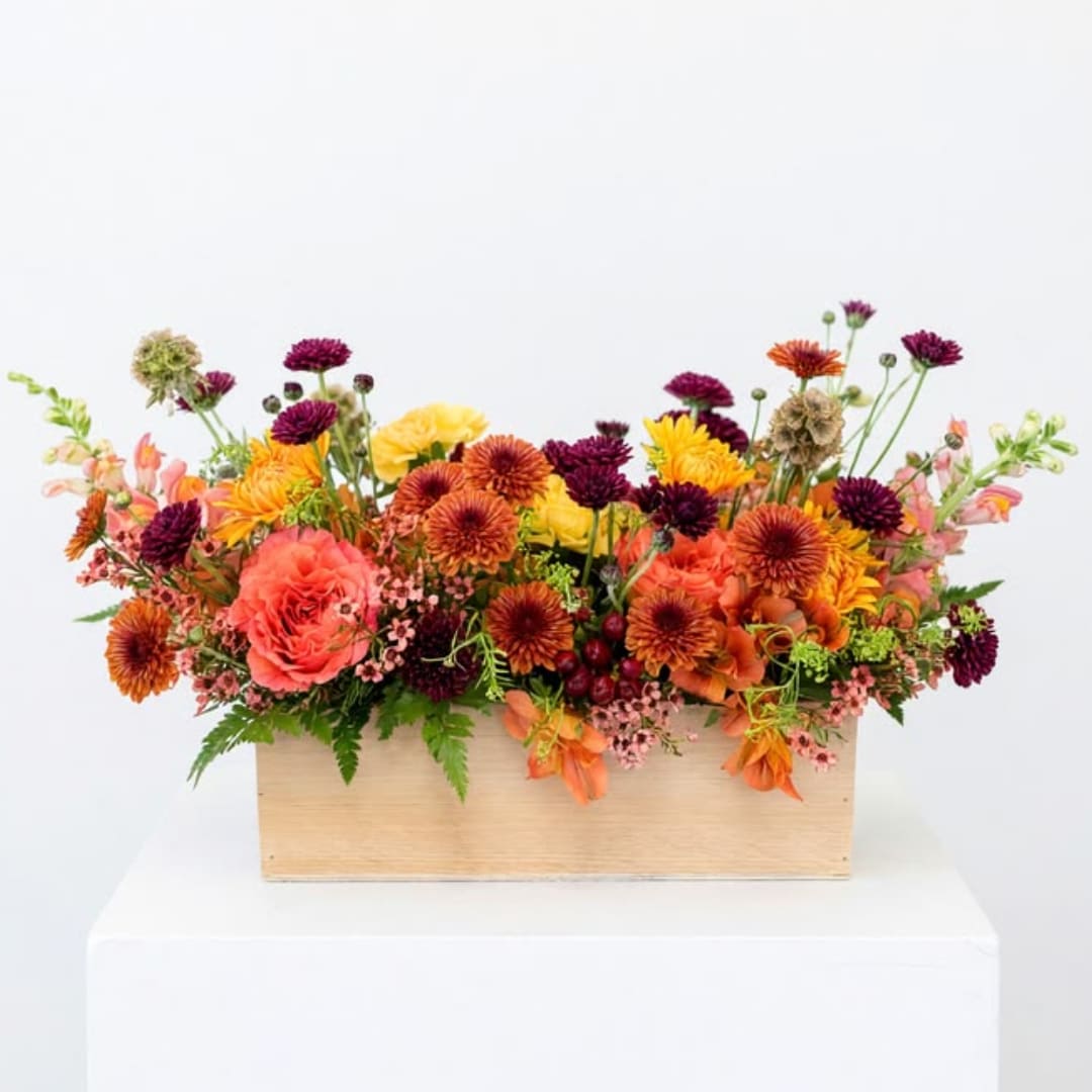 Mixed orange, pink, and purple flowers arranged in a wooden box