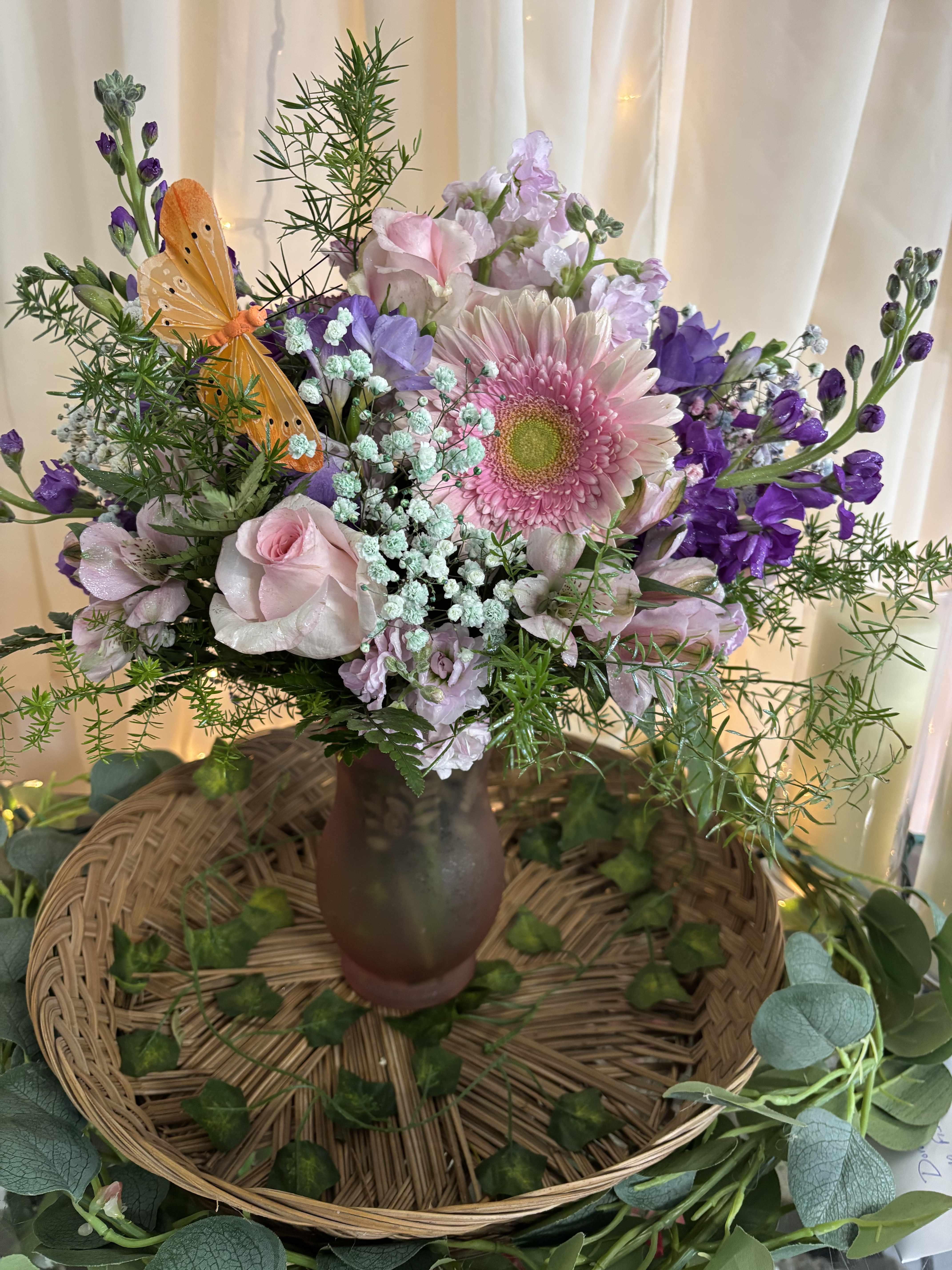 Pink and purple mixed bouquet in a brown vase with an orange butterfly