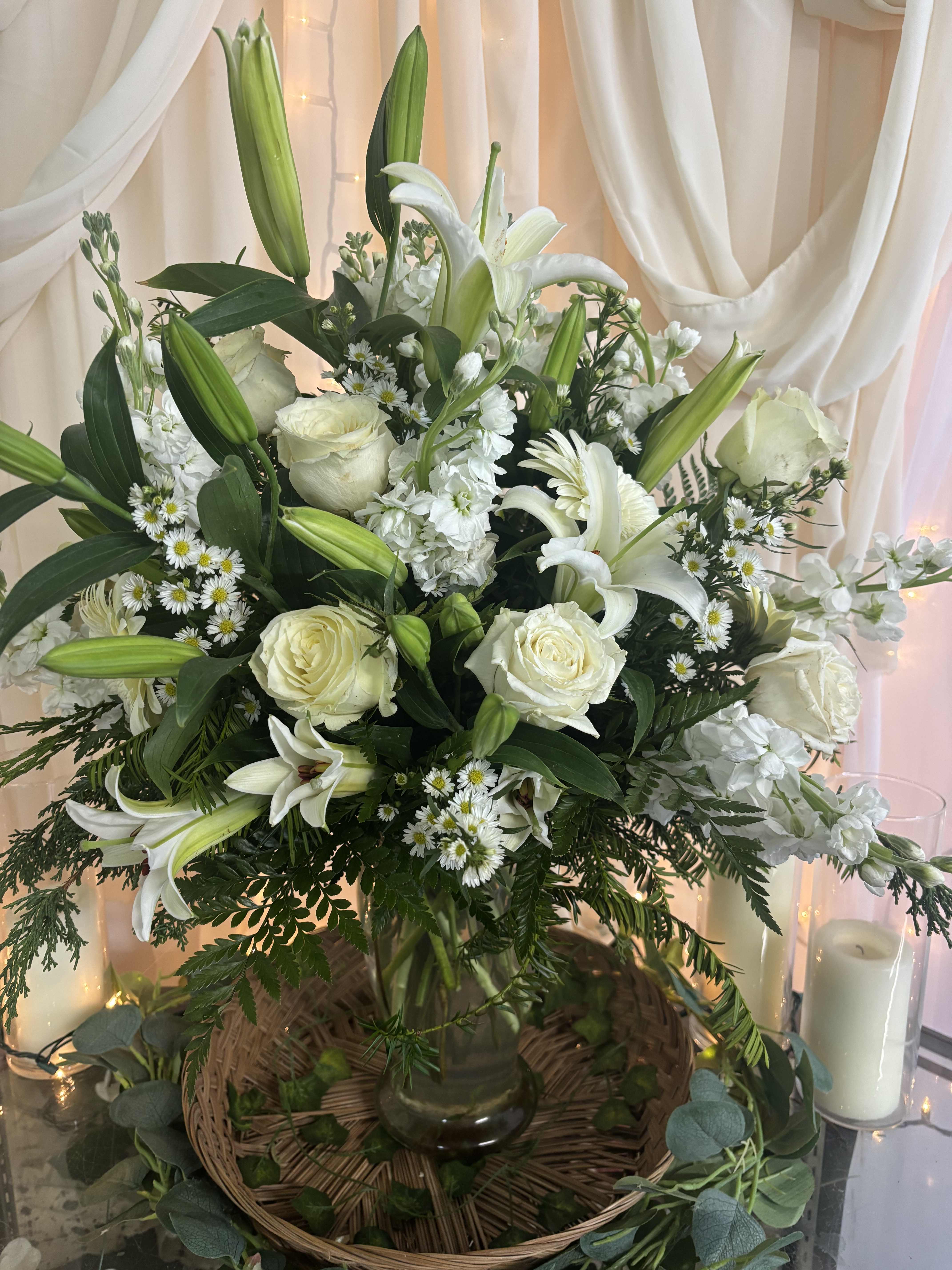 White lilies and roses arranged in a glass vase with greenery