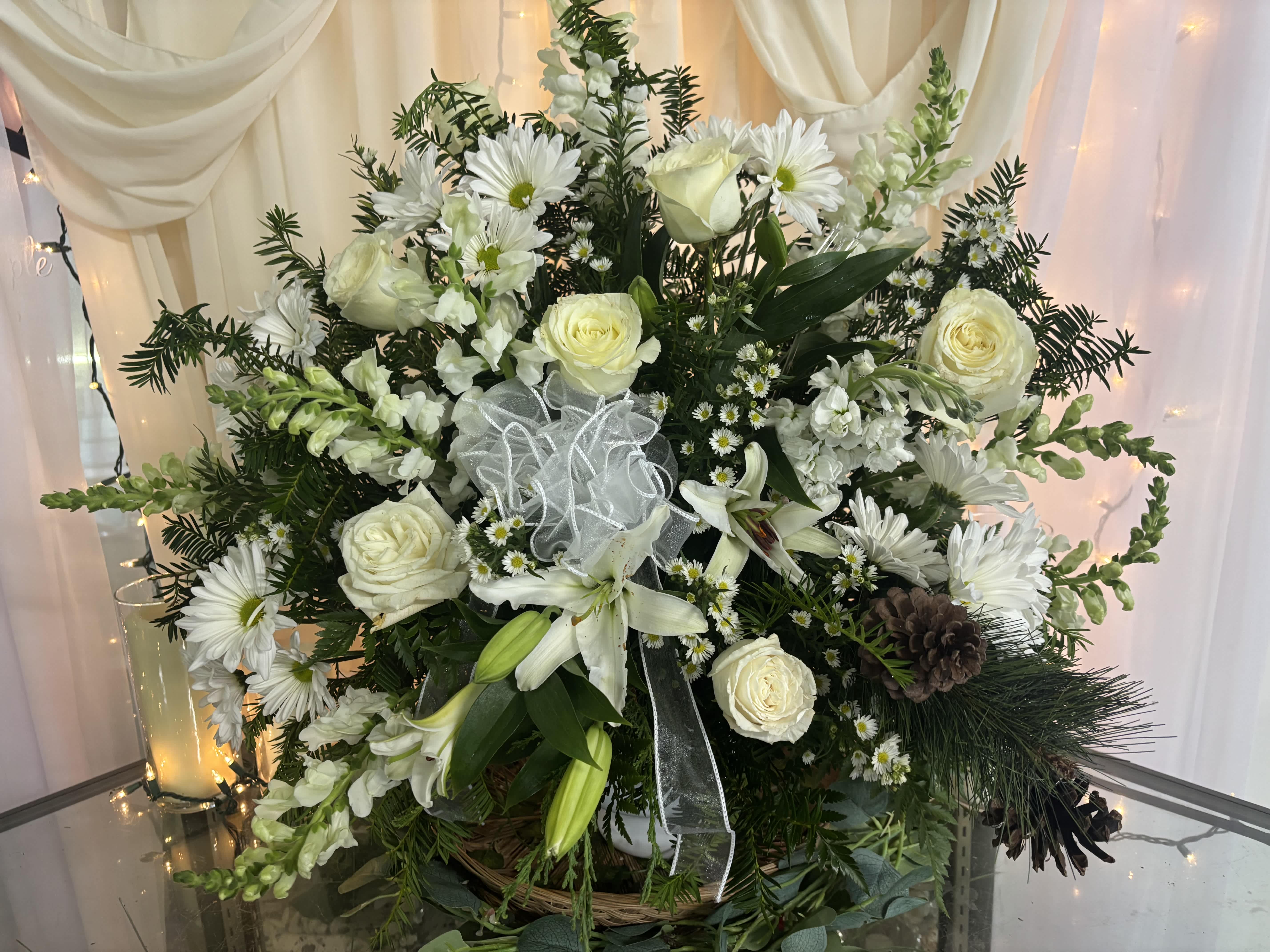 White roses and daisies arranged in a basket with a sheer ribbon