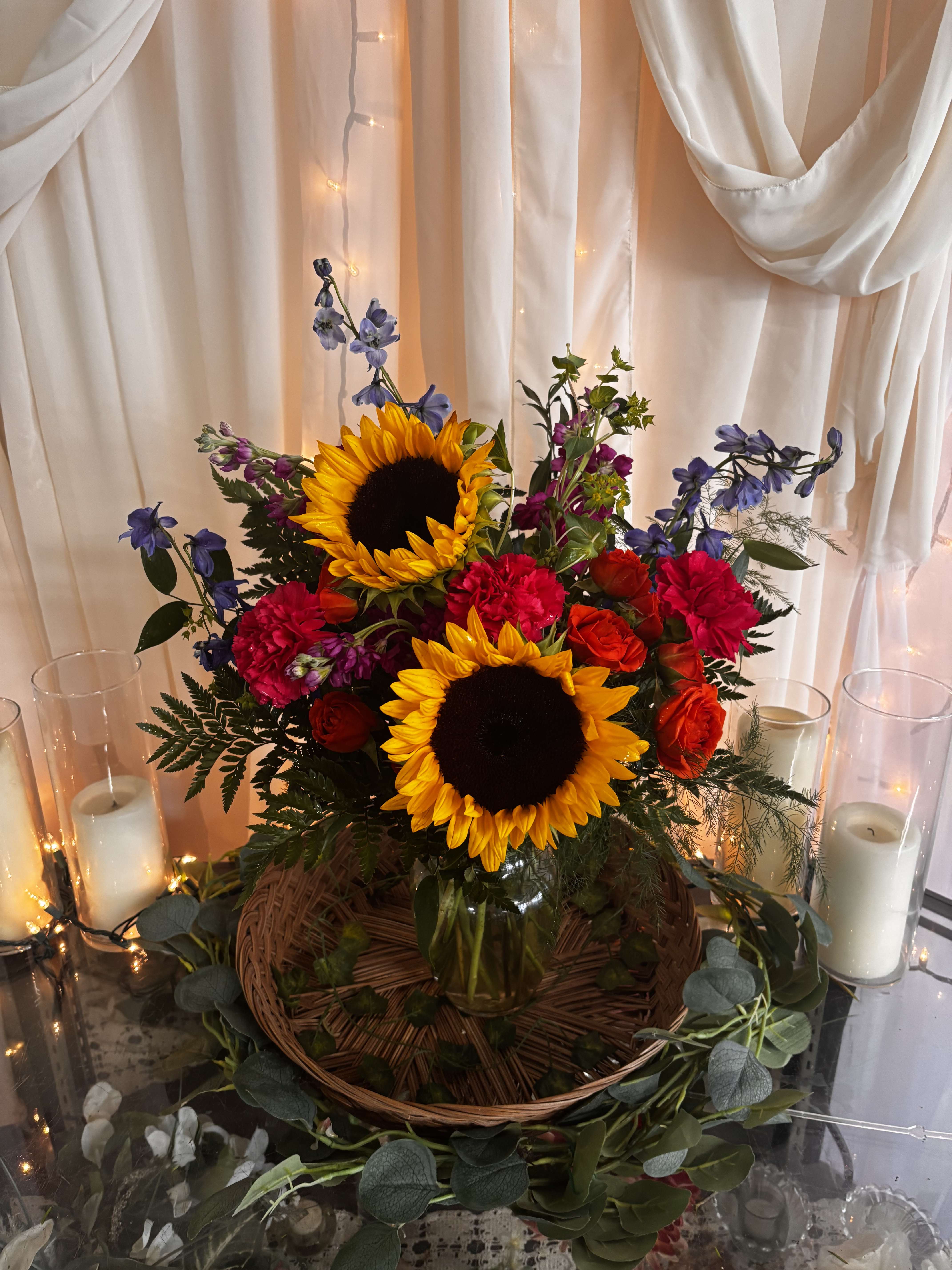 Sunflowers, red roses, and purple flowers in a glass vase