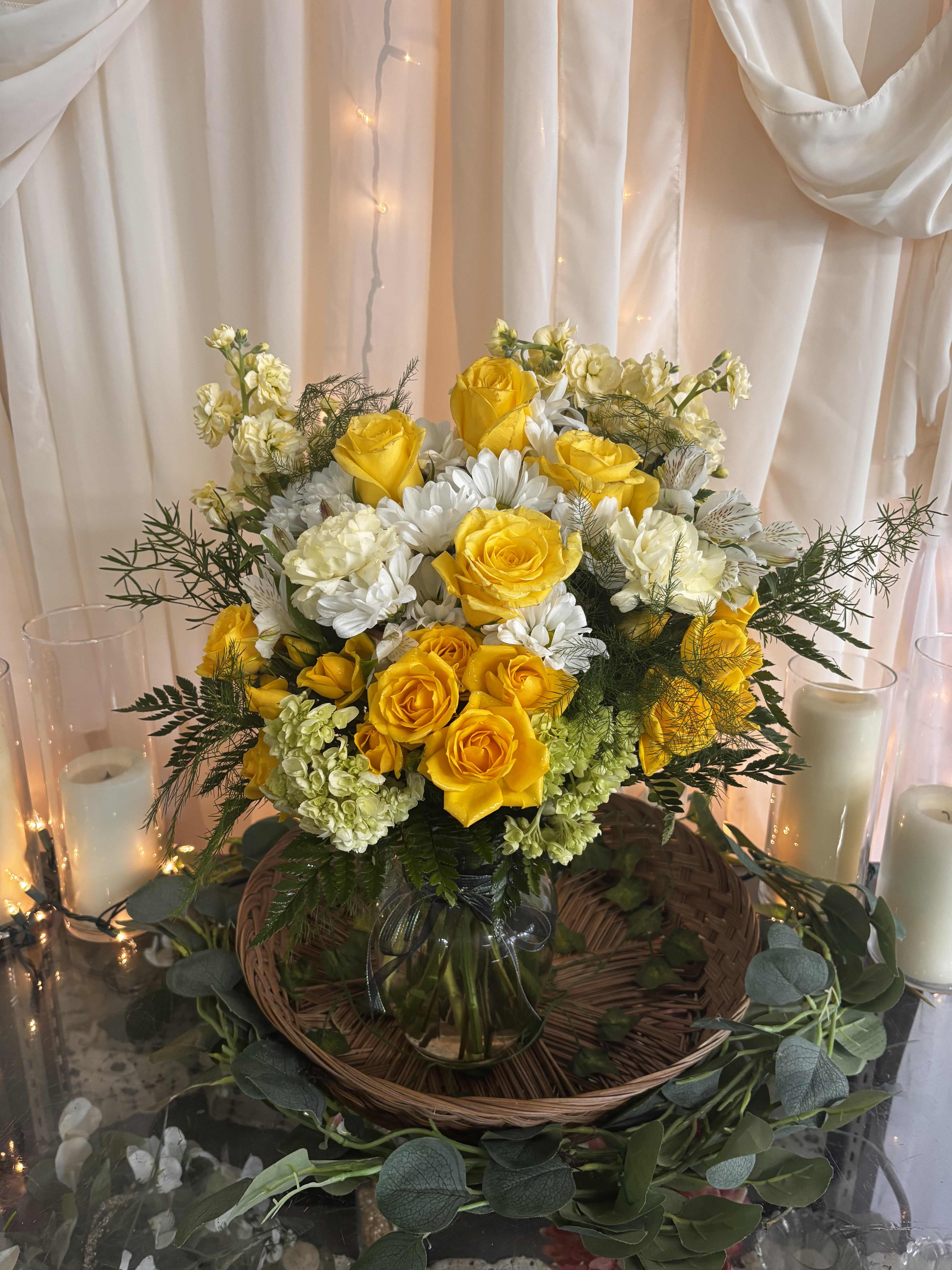 Yellow roses and white flowers in a glass vase with candles