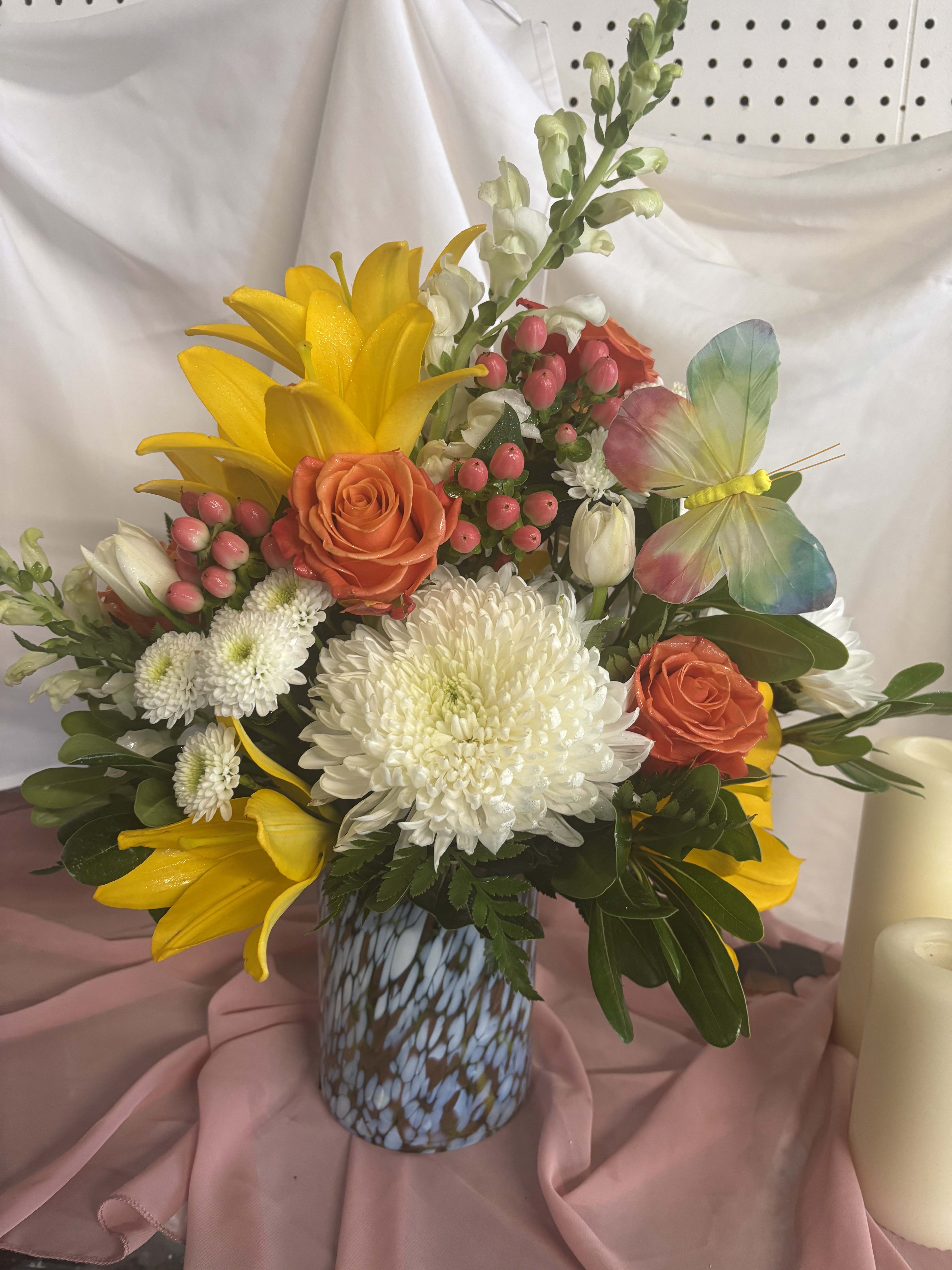 Mixed bouquet with yellow lilies, orange roses, and white chrysanthemums in a patterned vase