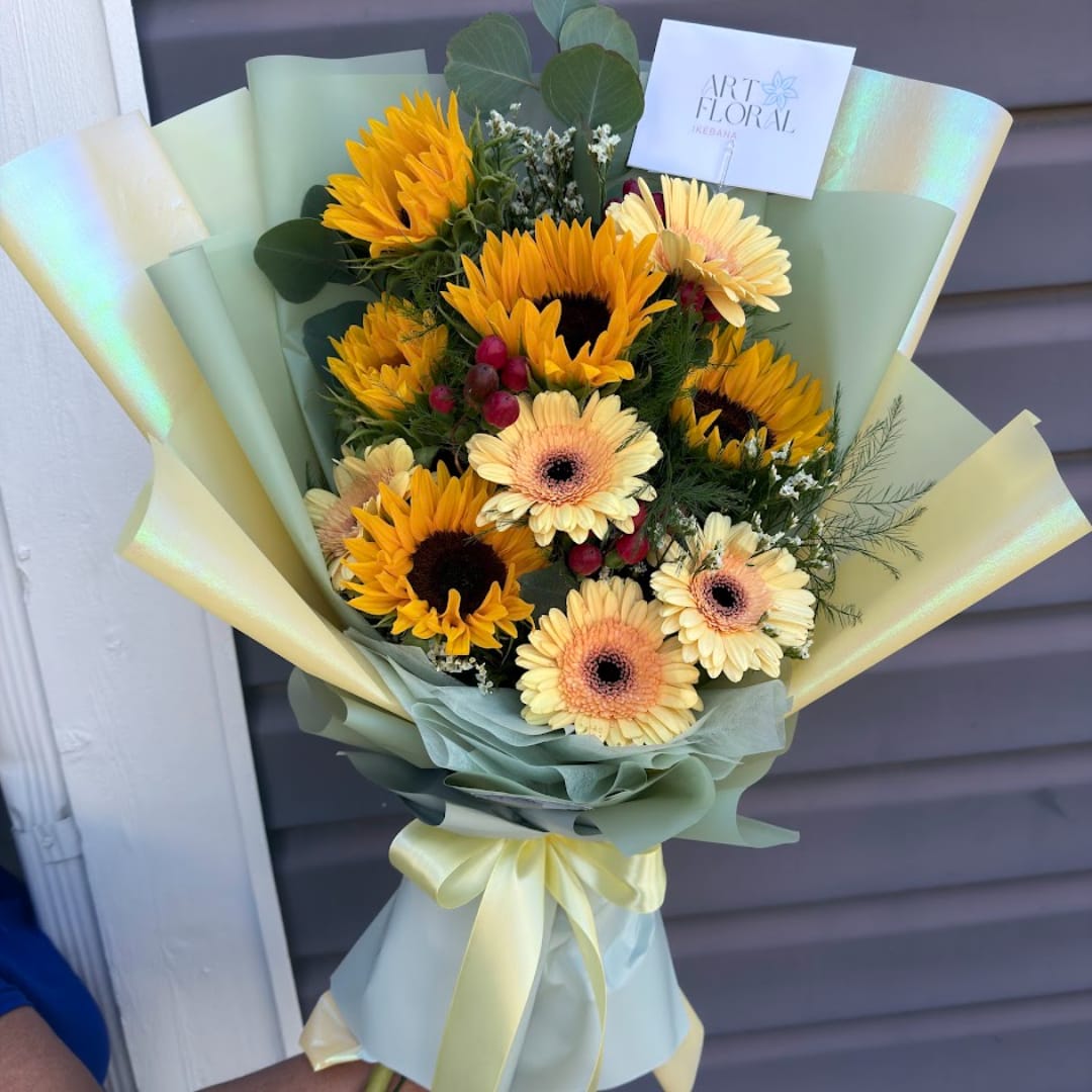 Bouquet of sunflowers and pale gerbera daisies wrapped in pastel paper