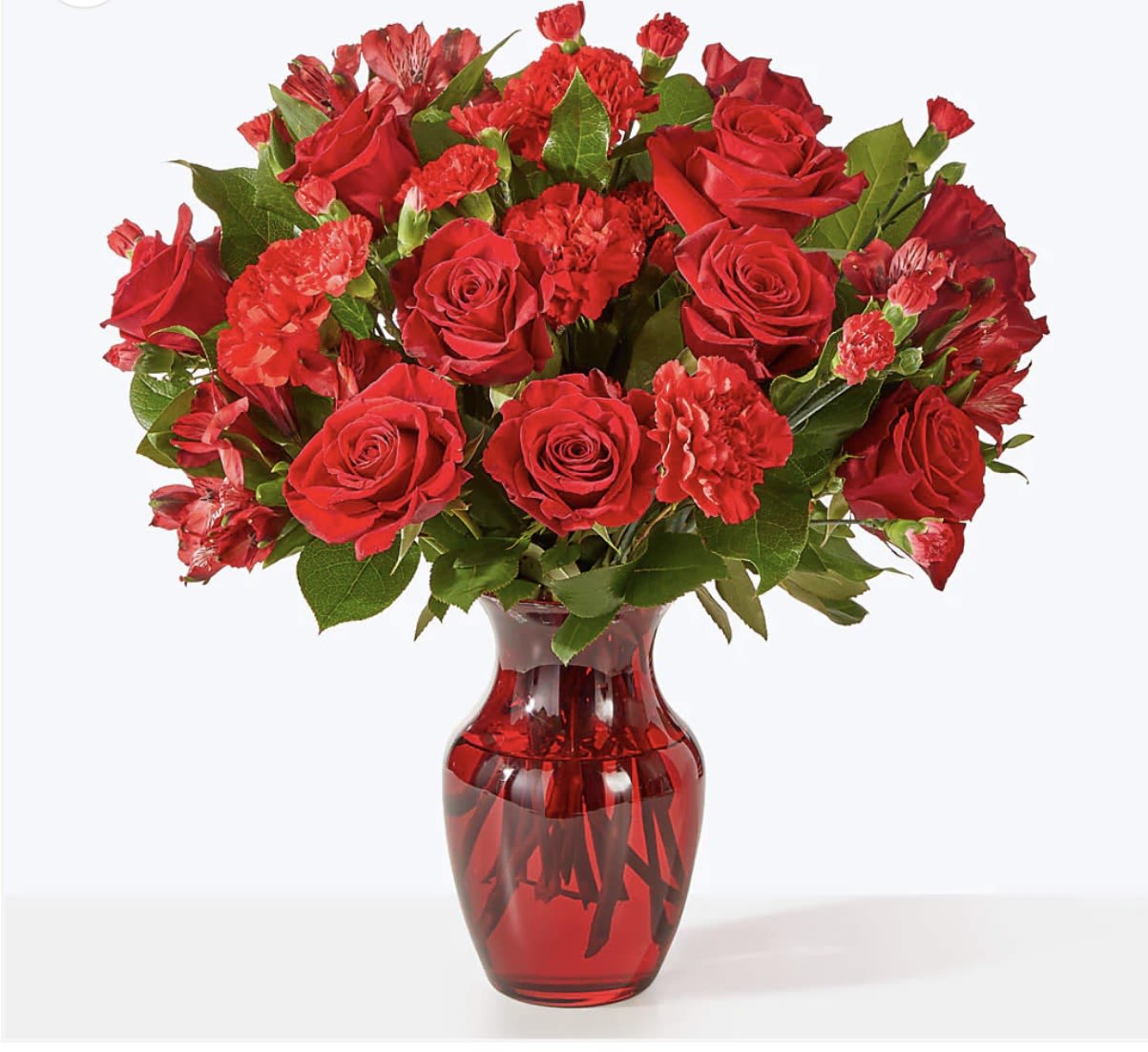 BIRTHDAY - A lush birthday bouquet that reads like two beautiful moods in one - choose the rich, romantic cluster of red roses and carnations for an anniversary or Valentine's Day vibe, or the soft pastel mix of peach, blush and white roses with a large pink chrysanthemum and airy blue delphinium for a gentle birthday or spring celebration. As a birthday flower arrangement, this selection sends a clear message: she'll feel cherished and celebrated, whether you want dramatic romance or tender, garden-fresh charm.  The red option is tightly rounded with dense red roses and carnations nestled against broad green foliage, presented in a translucent red glass vase for a bold, monochromatic statement with glossy contrast. The pastel version pairs peach, white and blush roses with a focal pink chrysanthemum, delicate blue delphinium-like blooms and loose eucalyptus and mixed greenery in a clear glass vase, creating a soft, textured silhouette. Both styles come in a classic glass vase that keeps stems hydrated and the arrangement looking finished on arrival.  Perfect for birthdays, anniversaries, thank-you gestures, or simply to let someone know you're thinking of them, these bouquets are designed to make the recipient feel genuinely seen. Order with standard sizing to fit a tabletop or select any available upgrades for a larger presentation; keep flowers in fresh water, trim stems and refresh water every couple of days to extend their vase life.