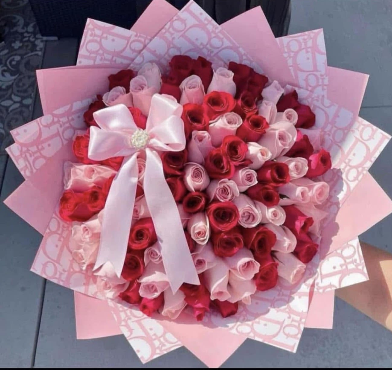RAMOS BUCHONES - A lush dome of red and pink roses makes a bold romantic statement for an anniversary bouquet, Valentine's Day gift, or a birthday surprise-this hand-tied flower arrangement reads like a kiss at first glance. The dense, rounded shape and rich red-and-pink palette ensure the person you're thinking of will feel adored and celebrated the moment they see it.  Tightly packed roses create a full, soft-textured surface framed in layered pink decorative wrapping paper with a pale patterned liner for an elegant contrast. A large white satin ribbon bow at the front adds a polished, present-like finish that keeps the focus on the blooms while elevating the gift-ready look.  Perfect for signaling love, admiration, or heartfelt congratulations, this arrangement arrives ready to set on a table or bedside-no extra fuss required. Care: replace water daily and trim stems if placing into a vase to extend freshness; select delivery timing at checkout to ensure it arrives on the special day.