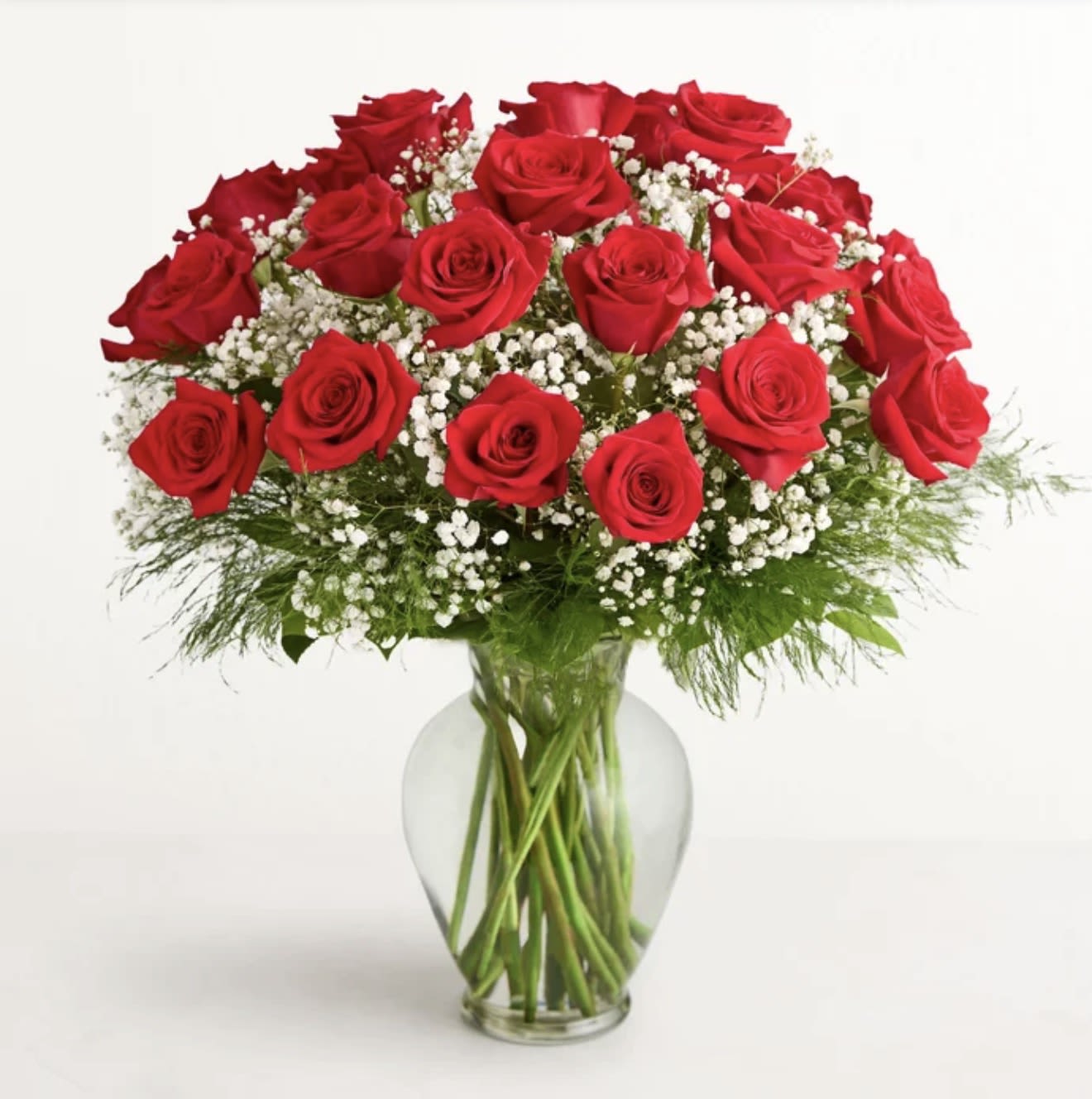 RAMO LOVE - A dense cluster of richly saturated red roses gathered into a rounded bouquet makes a bold, romantic statement-perfect as an anniversary roses arrangement or a Valentine's Day gift to show deep affection. The classic red-and-white palette and formal, full shape say "I love you" without words, making the person you're thinking of feel cherished and celebrated.  Each long-stem red rose is arranged tightly with small white filler flowers tucked throughout for bright contrast and soft texture. The stems sit in a clear glass vase that exposes the greenery and gives a clean, simple presentation; the overall silhouette is full and rounded for a timeless look. Ideal for anniversaries, romantic gestures, or everyday expressions of love-this arrangement arrives ready to display and will make her feel truly seen.
