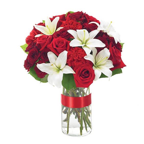 Red roses and white lilies in a clear glass vase with a red ribbon