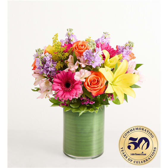 Mixed bouquet of roses, lilies, and daisies in a green glass vase