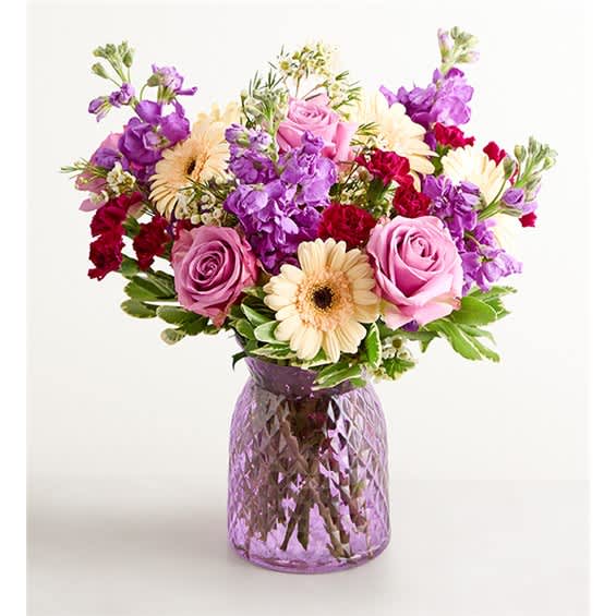 Mixed bouquet of pink, purple, and cream flowers in a purple glass vase