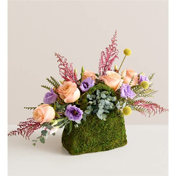 Peach roses and purple blooms in a moss-covered container