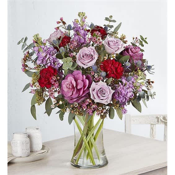 Mixed bouquet of pink, purple, and red flowers in a clear glass vase