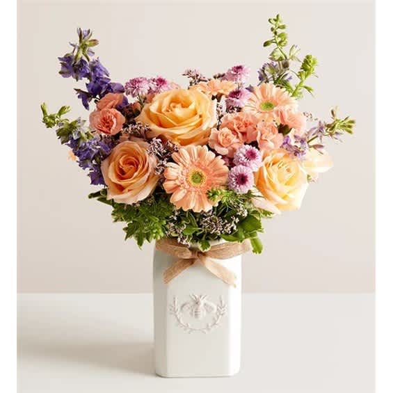 Mixed bouquet of peach roses and pastel daisies in a white vase