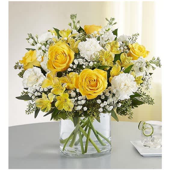 Yellow roses and white flowers arranged in a clear glass vase