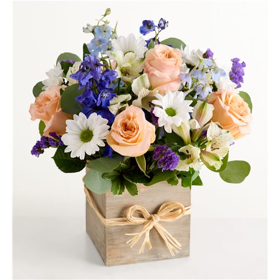 Mixed bouquet of peach roses, white daisies, and blue flowers in a wooden box